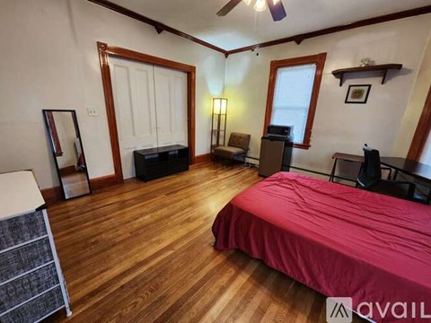 A bedroom with a red bedspread and wooden floors.