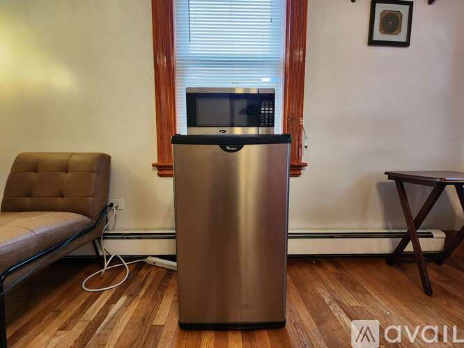 A silver fridge in a room with a brown chair and a small table.