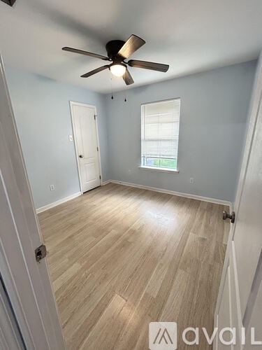 A room with a ceiling fan and light, hardwood floors, and a window with blinds.