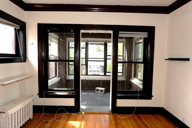 A room with a wooden floor and a large window with a view of a patio.
