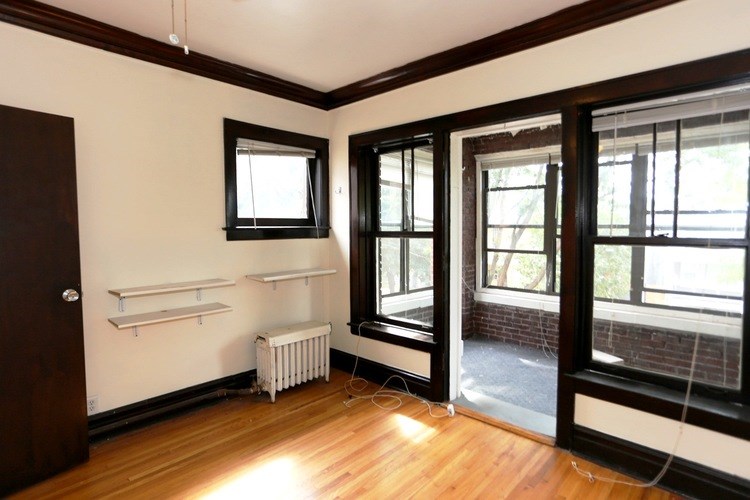 A room with a brown door, a window with a black frame, and a white radiator.