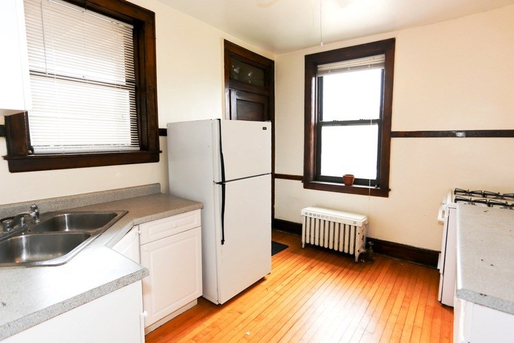 A kitchen with a white fridge and a window with blinds.