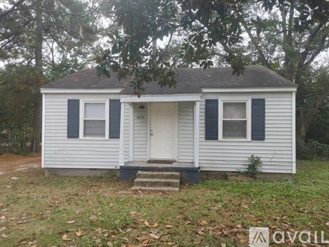A small white house with a black door and windows surrounded by trees.