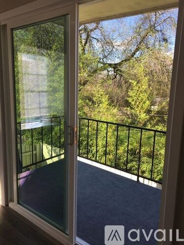 A balcony with a glass door leading to a lush green outdoor area.