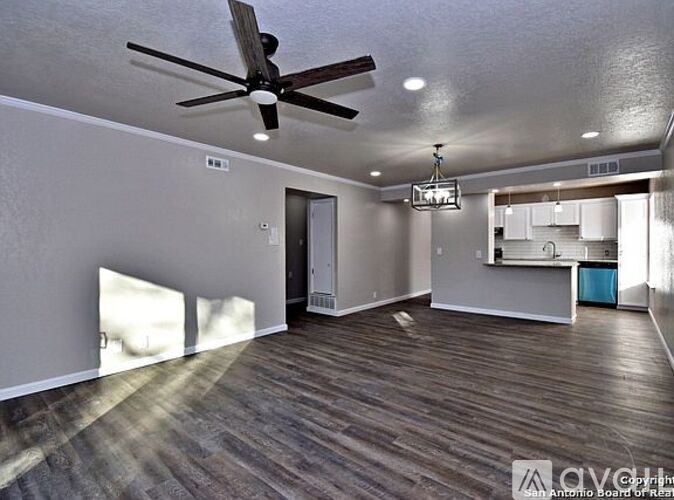 A room with a ceiling fan and a kitchen area in the background.