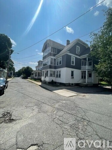 A large, two-story house with a grey and white exterior sits on a street with a cracked asphalt surface.
