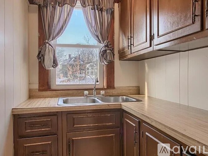 A kitchen with wooden cabinets and a window with curtains.