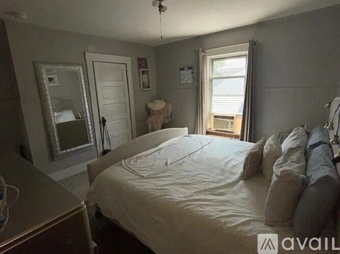 A bedroom with a bed, dresser, mirror, and window.