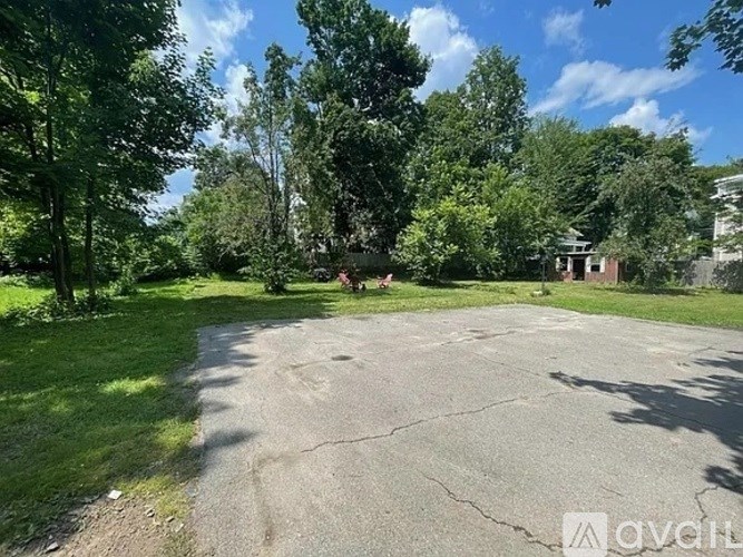 A large, empty parking lot surrounded by trees and a building in the distance.