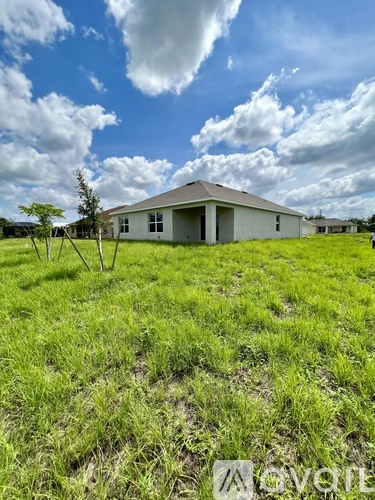 A single-story house with a grey roof and white walls is surrounded by a grassy field.
