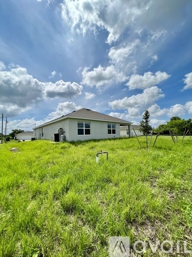 A house is situated in a grassy field with a partly cloudy sky above.