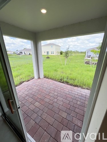 A patio with a brick floor and a view of a grassy field and houses.