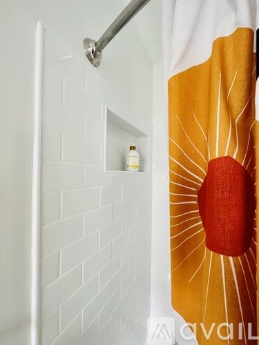 A shower curtain with a sun design hangs in a white tiled shower.