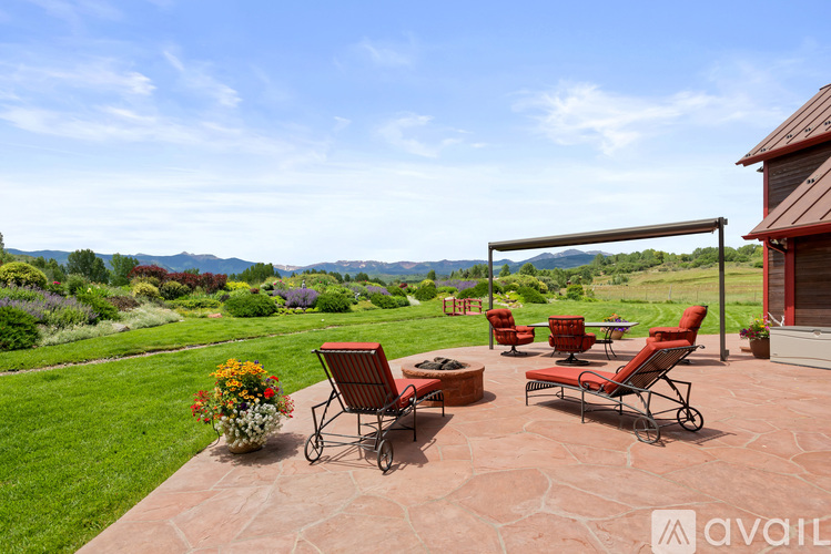 A patio with red chairs and a table is set up on a patio with a view of the mountains.
