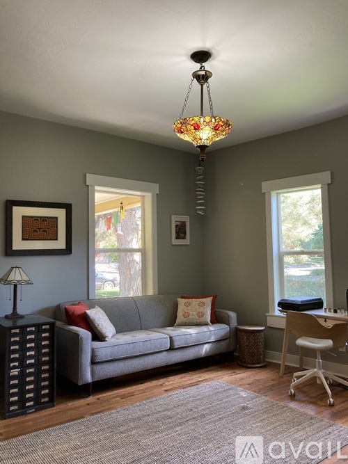 A living room with a grey couch, a lamp, a chandelier and a window.