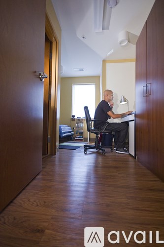 A man is sitting at a desk in a room with wooden floors and a window.