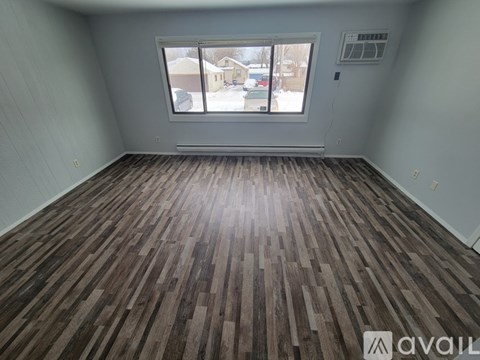 A room with wooden flooring and a window showing a view of a residential area.