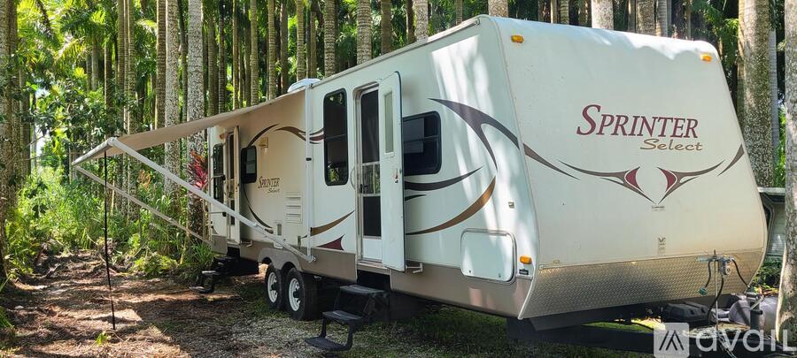A white RV with the word "Sprinter" on it is parked in a wooded area.