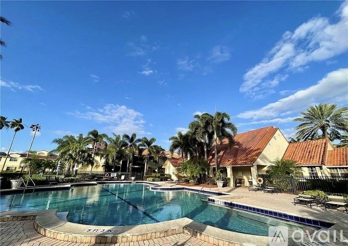 A pool surrounded by palm trees and a building with a red roof.