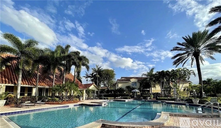 A pool surrounded by palm trees and a building in the background.