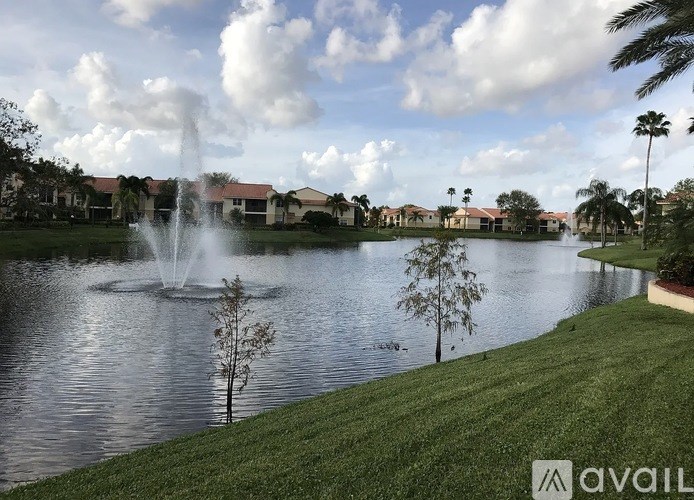 A fountain in the middle of a lake surrounded by trees and buildings.