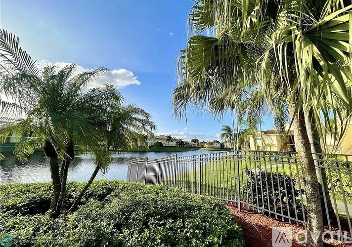 A fence with a sign that says "KOVEN" is in front of a body of water with palm trees.