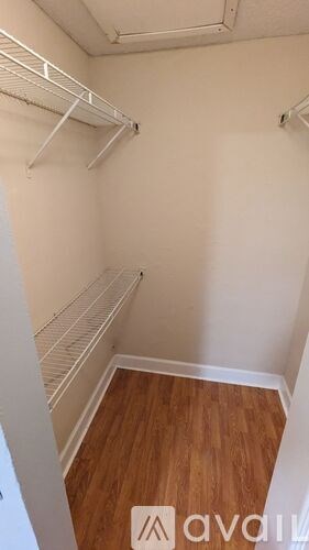 A room with white walls and wood flooring with a white shelf on the wall.