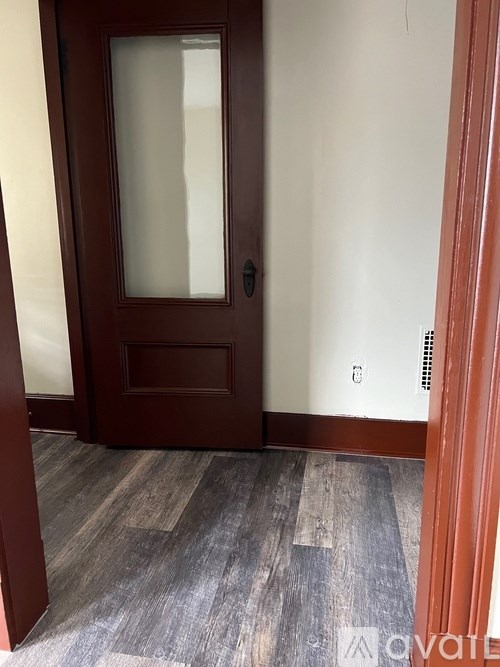A brown door with a glass window is in a room with wooden flooring.