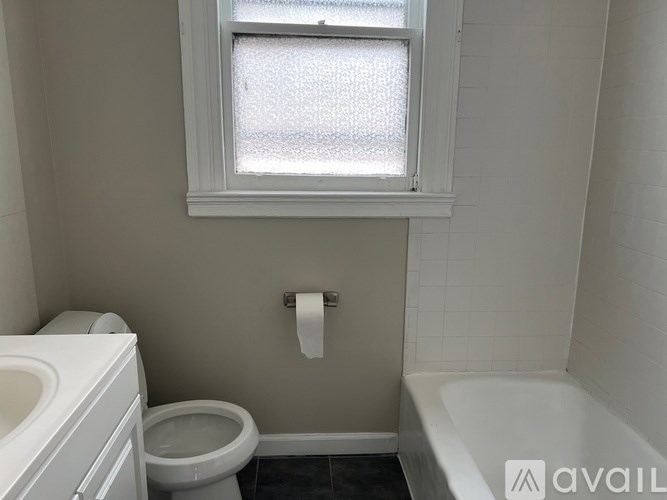 A white toilet sits next to a white bathtub in a bathroom with a window.