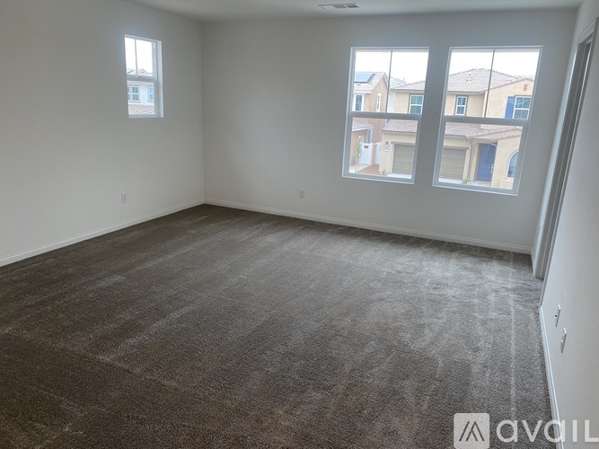 A room with grey carpet and two windows overlooking a residential area.