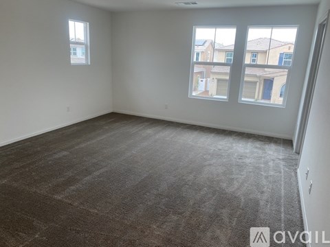 A room with grey carpet and two windows overlooking a residential area.
