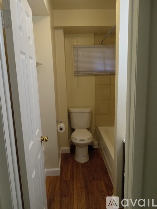A white toilet in a small bathroom with wooden floors.