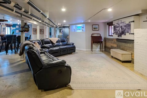 A living room with a black leather couch and a rug on the floor.