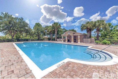 A swimming pool surrounded by a brick border with a house in the background.