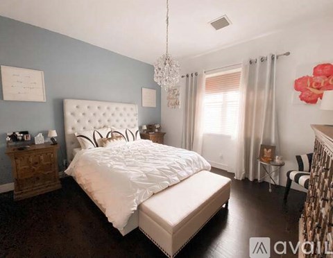A bedroom with a large bed, a chandelier, and a chair.