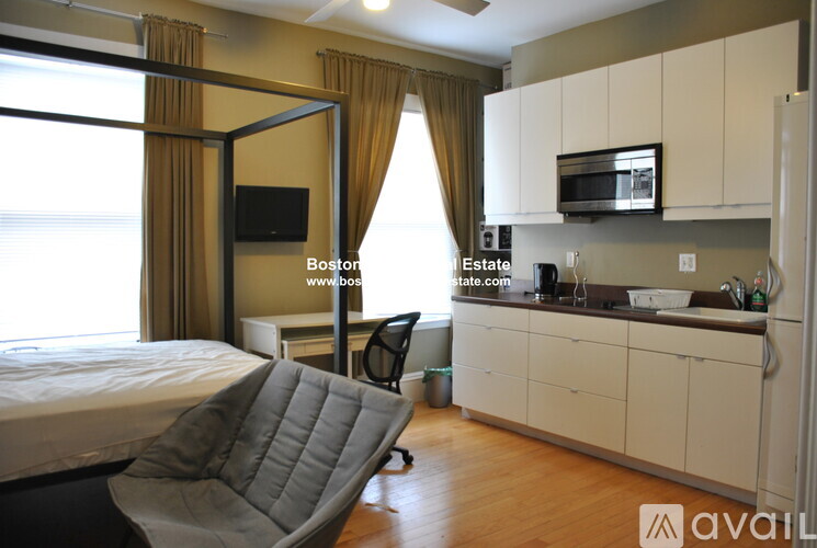 A bedroom with a bed, chair, and a kitchenette area.
