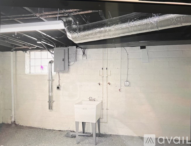 A white sink in a room with pipes and ducts.