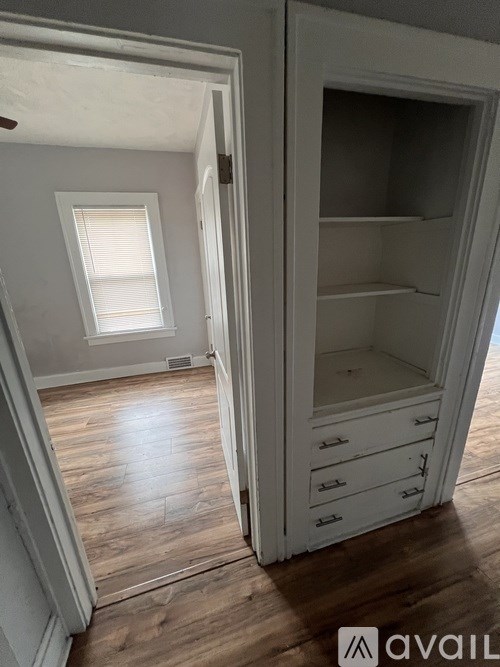 A white cabinet with drawers is open in a room with wooden floors.