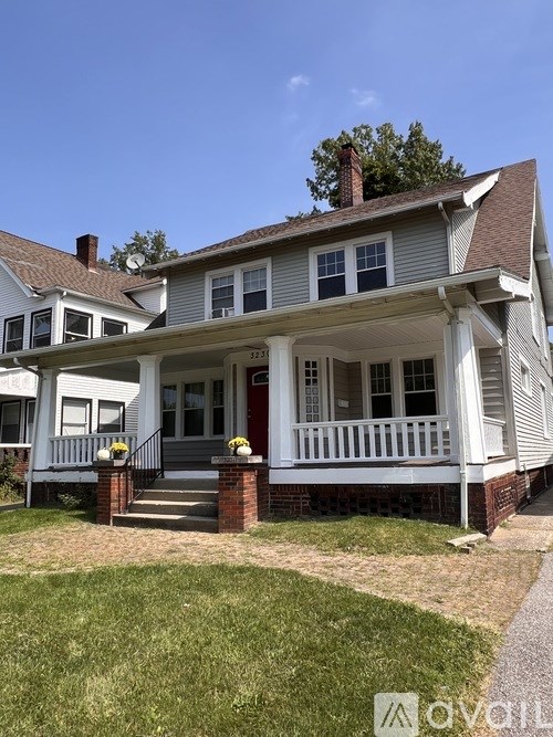 A two-story house with a porch and a brick chimney.