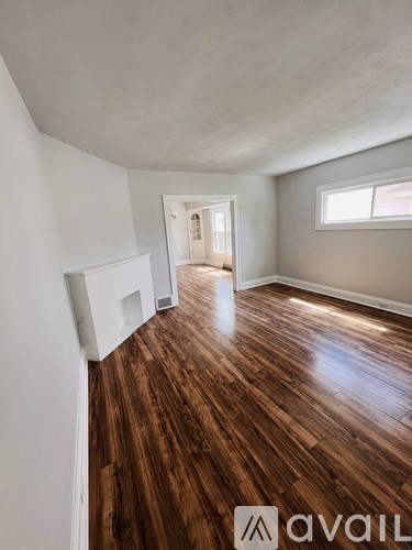 A room with wooden floors and white walls, with a doorway leading to another room.