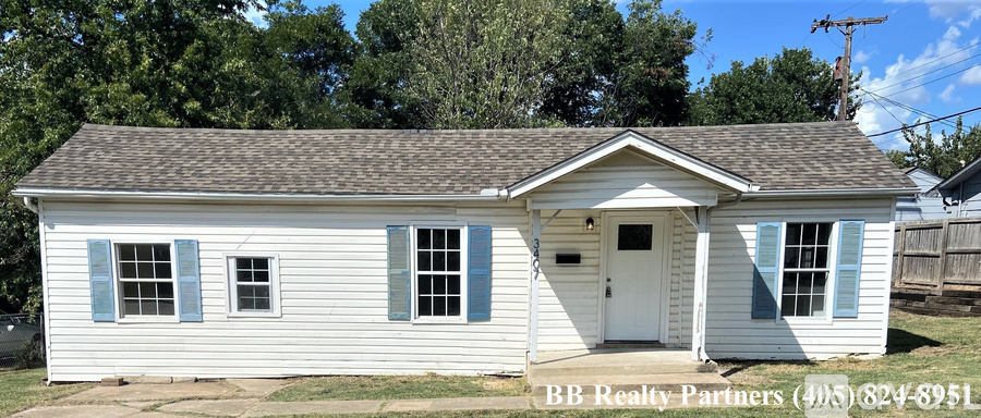 A small white house with a brown roof and a BB Realty Partners sign in front.