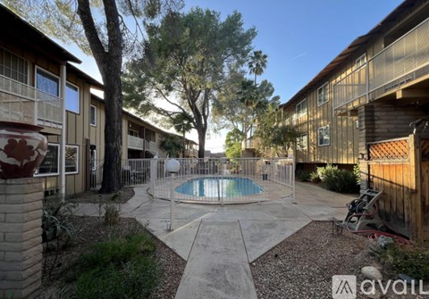 A pool surrounded by a concrete patio and a fence with a tree in the background.