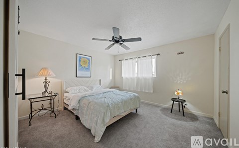 A bedroom with a bed, a fan, and a lamp.