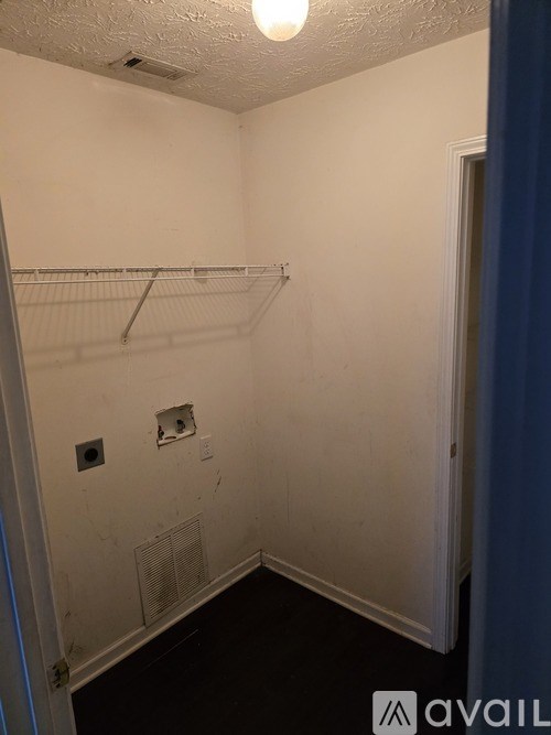 A small, empty room with a white wall and a metal vent.