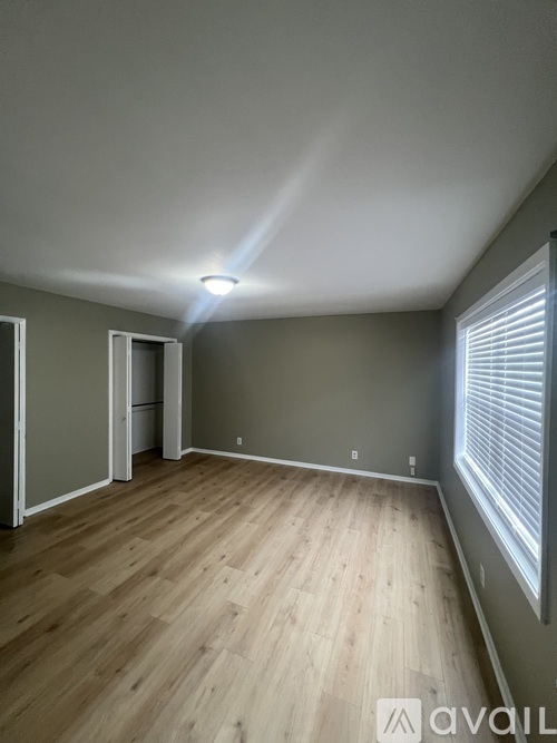 A room with wooden flooring and a window with blinds.