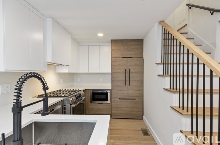 A modern kitchen with a stainless steel sink and wooden staircase.