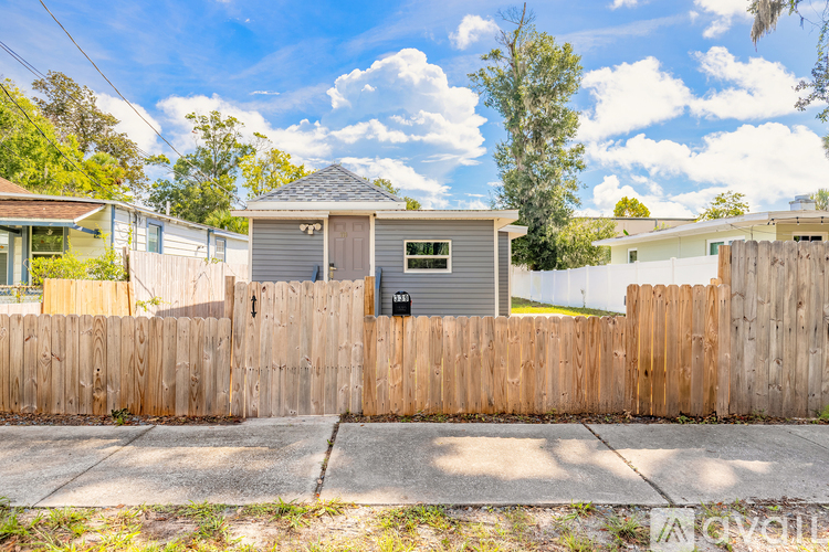 A small house with a grey roof is surrounded by a wooden fence.