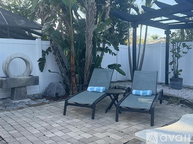 Two chairs are placed on a patio with a white wall and a tree in the background.