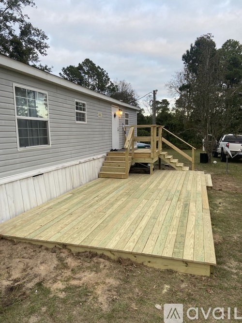 A wooden deck is in front of a grey house.