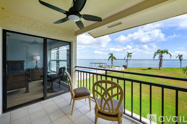 A balcony with a chair and a ceiling fan overlooking a grassy area with palm trees.